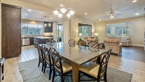Un comedor amplio con una gran mesa y sillas, una cocina al fondo y una sala de estar con un sofá y un televisor.