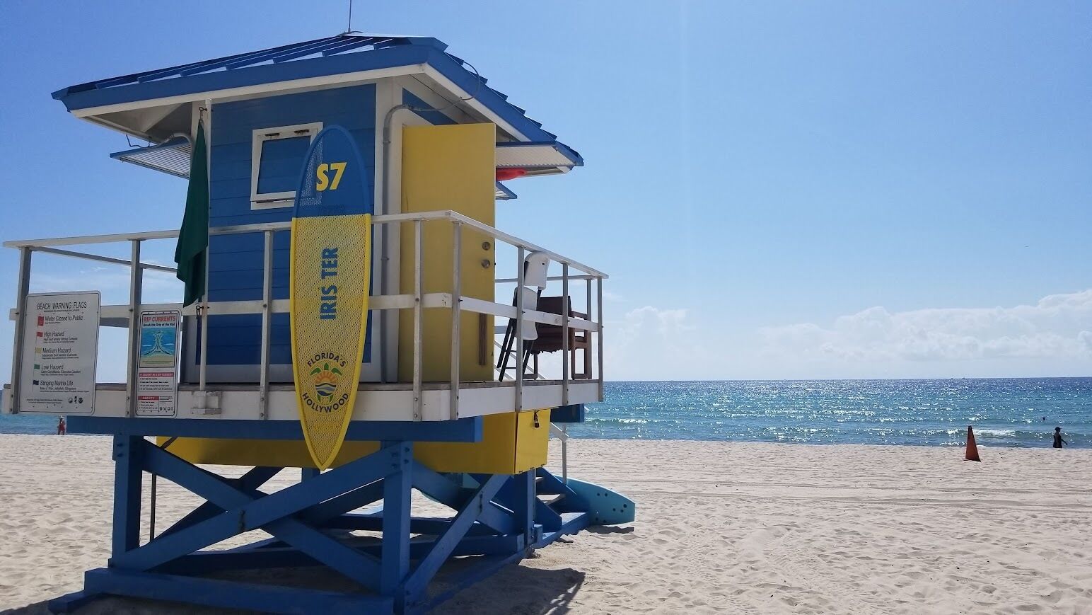 A lifeguard tower with the number S7, a beach warning sign, and a flag indicating a medium hazard level.