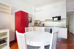 Una cocina pequeña con armarios blancos, un refrigerador rojo y un comedor con sillas blancas.
