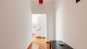 A hallway with a wooden floor, a black table with a plate, and a kitchen area in the background. - GuestHost - Cà Granda M5 & Bicocca - Apartment Cosy (Milano)