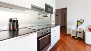A modern kitchen with a coffee maker, oven, microwave, and a fan on a stand. - GuestHost - Cà Granda M5 & Bicocca - Apartment Cosy (Milano)