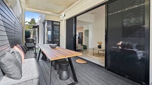Une terrasse moderne avec une table et des sièges en bois, une porte-fenêtre coulissante et une vue sur l’intérieur.
