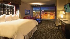Habitación de hotel con una cama grande, un escritorio, un televisor y vistas a la ciudad.