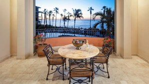 A round table with four chairs, a decorative bowl, and two glasses on a balcony overlooking a beach with palm trees and a fence. - 3BR Close to Beach overlooks pool and Sea! (Cabo San Lucas)