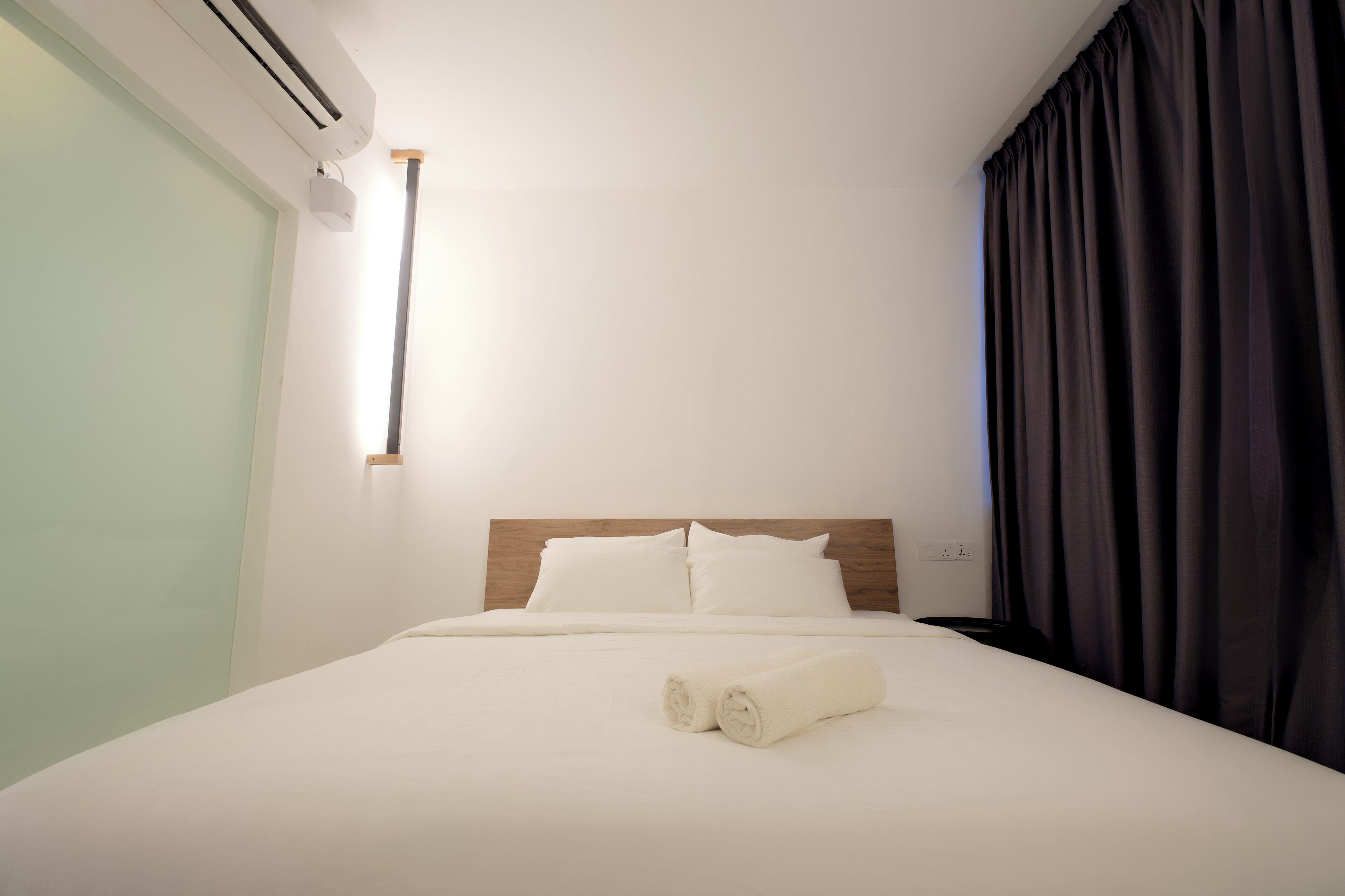 Una habitación de hotel con cama, ropa de cama blanca, cabecera de madera, aire acondicionado de pared y una ventana con cortinas.