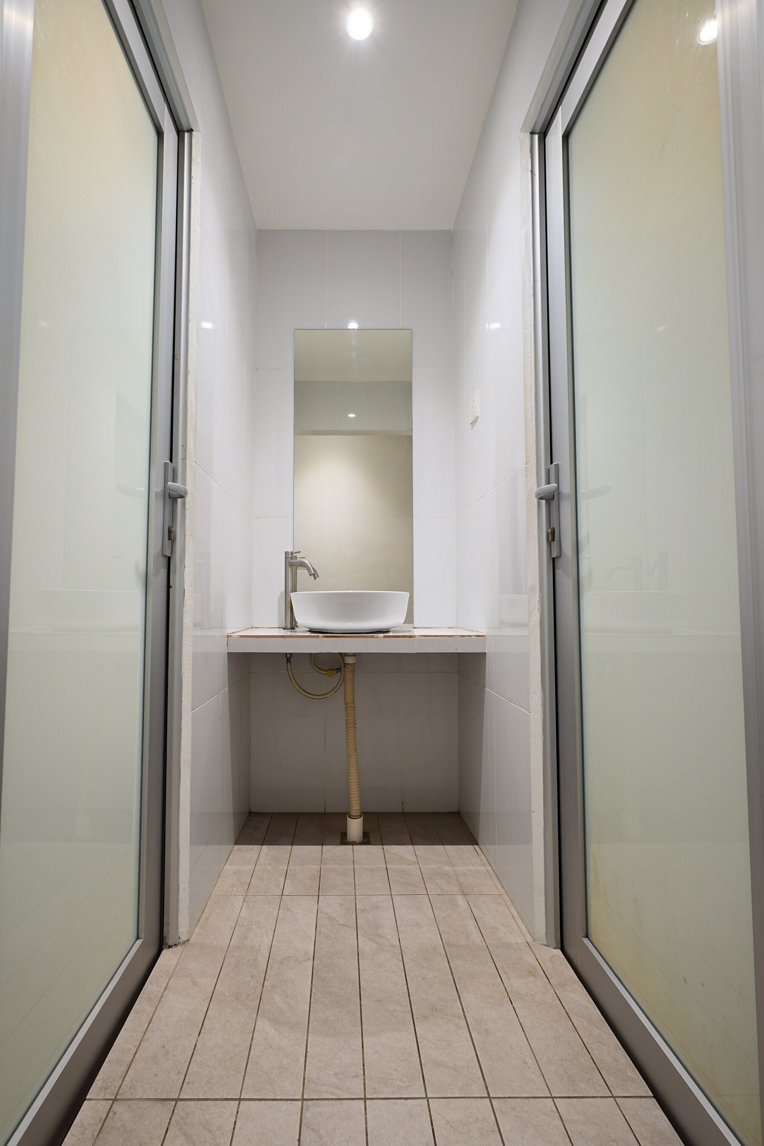 A narrow bathroom with a white sink, a mirror, and tiled flooring.