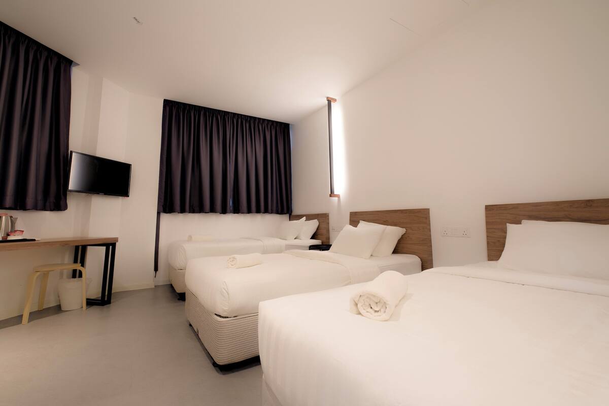 A hotel room with two beds, a desk, a television, and a large window with curtains.