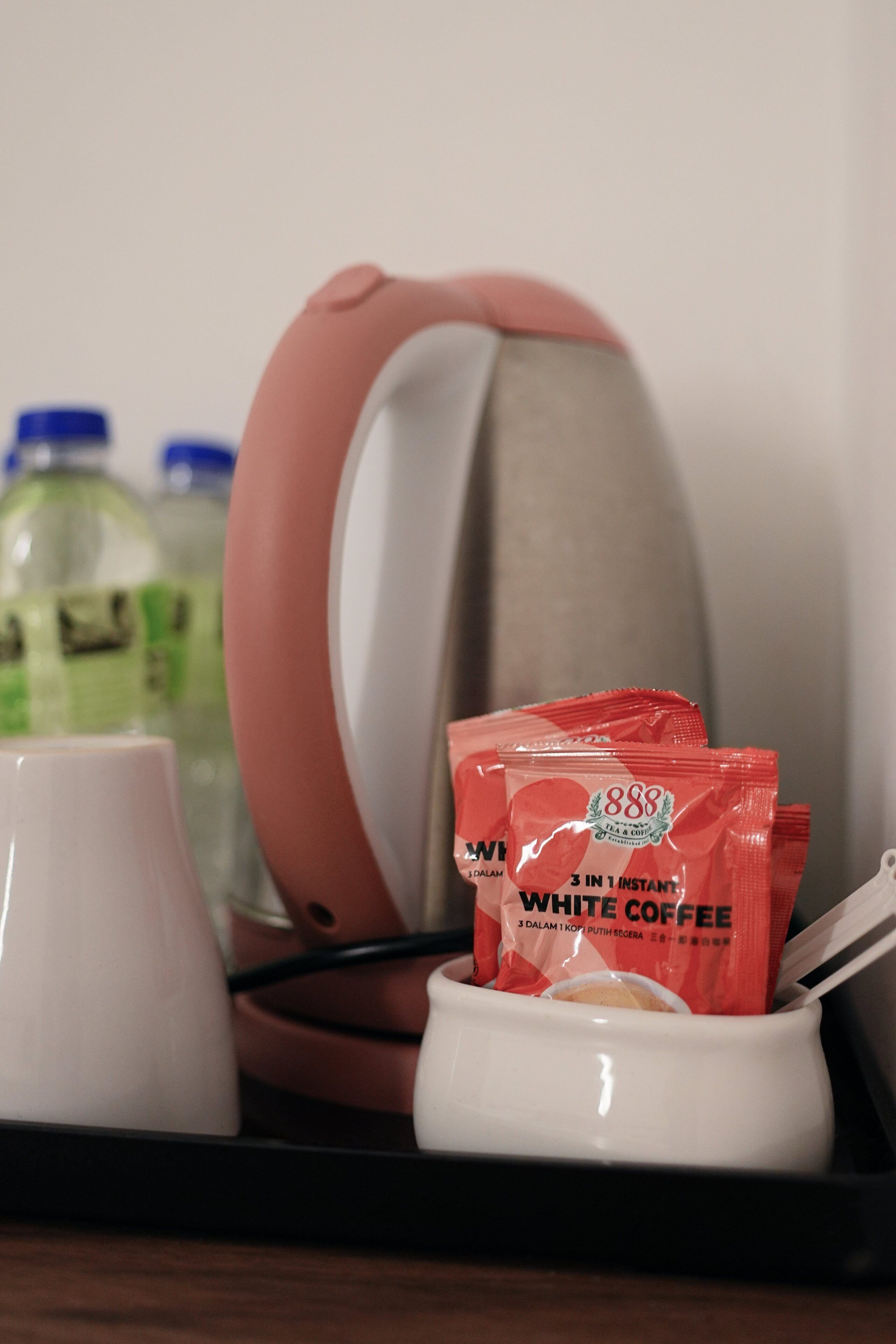Una bandeja con una cafetera blanca, una cafetera rosa y dos sobres de café.