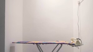 A corner room with a white wall, a small ironing board with an iron, and a power outlet. - T Hotel Jalan Sultanah (Alor Setar)