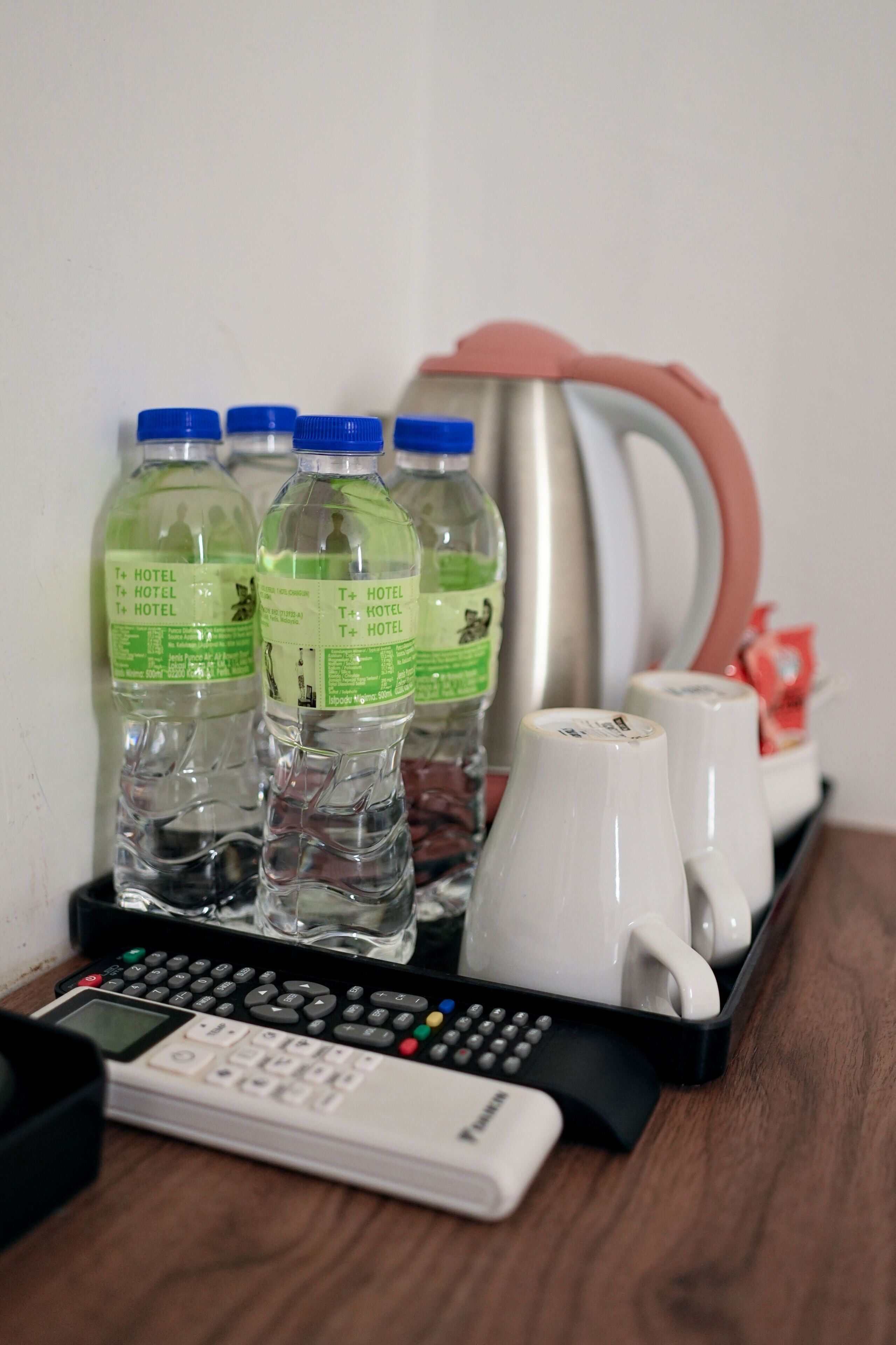 Quarto de hotel com minibar contendo água engarrafada, cafeteira e controle remoto.