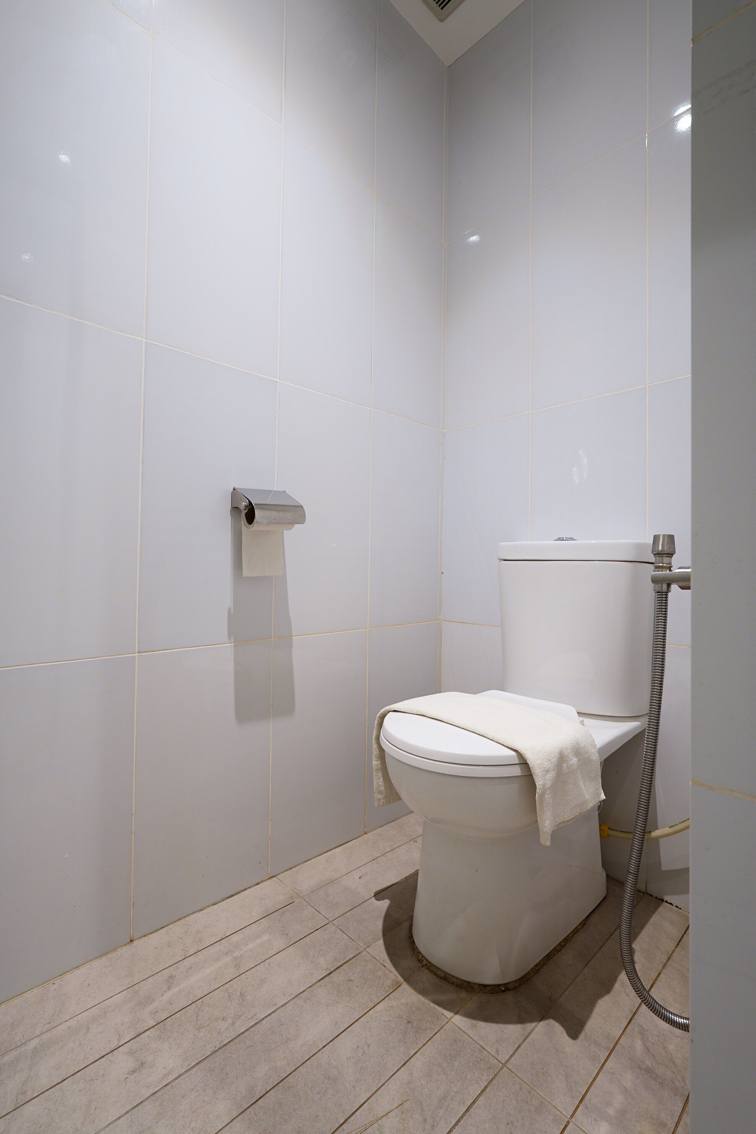 A modern bathroom with a toilet, a paper towel dispenser, and a shower hose.