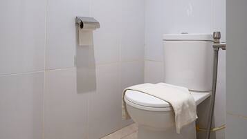 A modern bathroom with a toilet, a paper towel dispenser, and a shower hose.