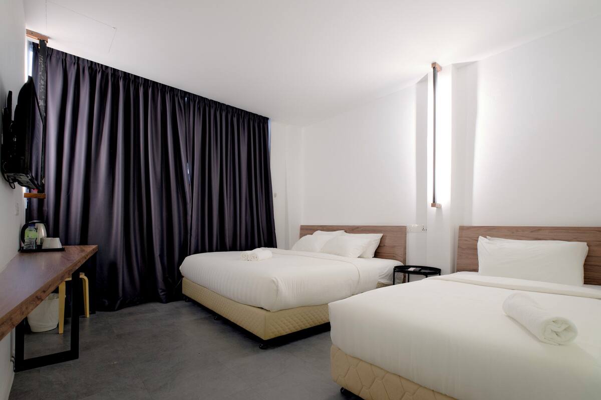 A hotel room with two beds, a desk, a chair, and a large window.
