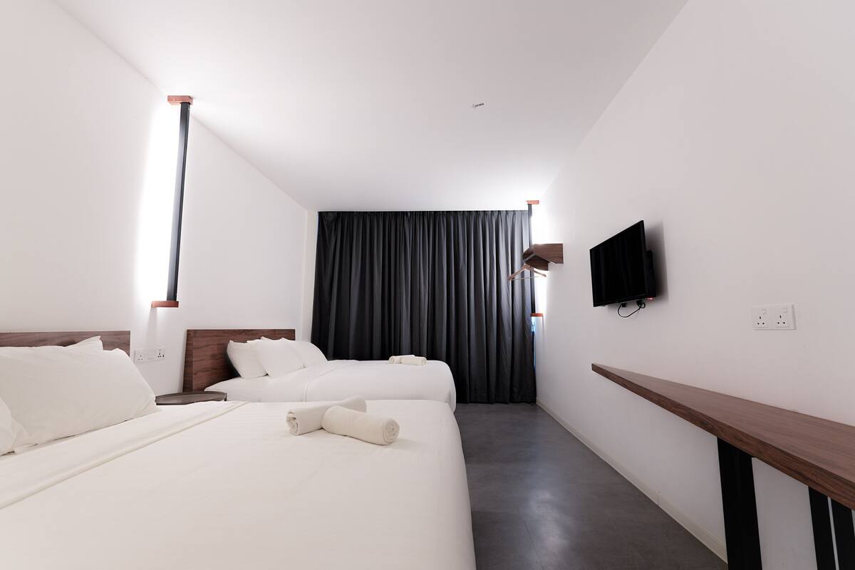 A hotel room with two beds, a flat-screen TV mounted on the wall, and a wooden bench.
