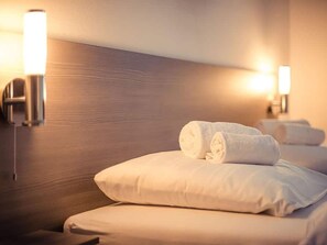 Habitación de hotel con una cama bien tendida, dos almohadas y dos lámparas de pared que ofrecen una luz suave.