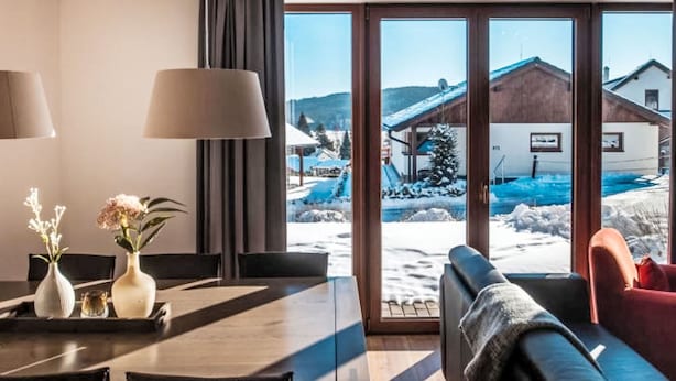 A modern hotel room with a dining area, a sofa, and a view of a snowy landscape with buildings. - Residence Lipno by Interhome (Lipno nad Vltavou)