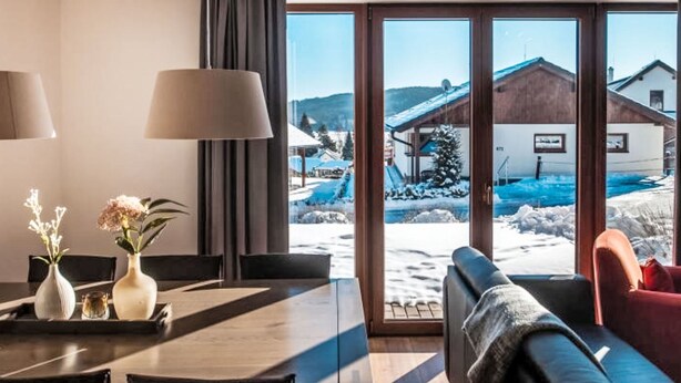 A modern hotel room with a dining area, a sofa, and a view of a snowy landscape with buildings. - Residence Lipno by Interhome (Lipno nad Vltavou)