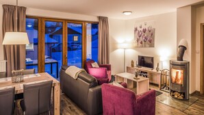 A cozy living room with a sofa, chairs, a TV, a fireplace, and a dining area with a table and chairs. - Residence Lipno by Interhome (Lipno nad Vltavou)