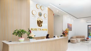 A hotel reception area with a modern design, featuring a reception desk, a receptionist, and a seating area with a sofa and armchairs. - Rosetta Hotel (Phu Quoc)
