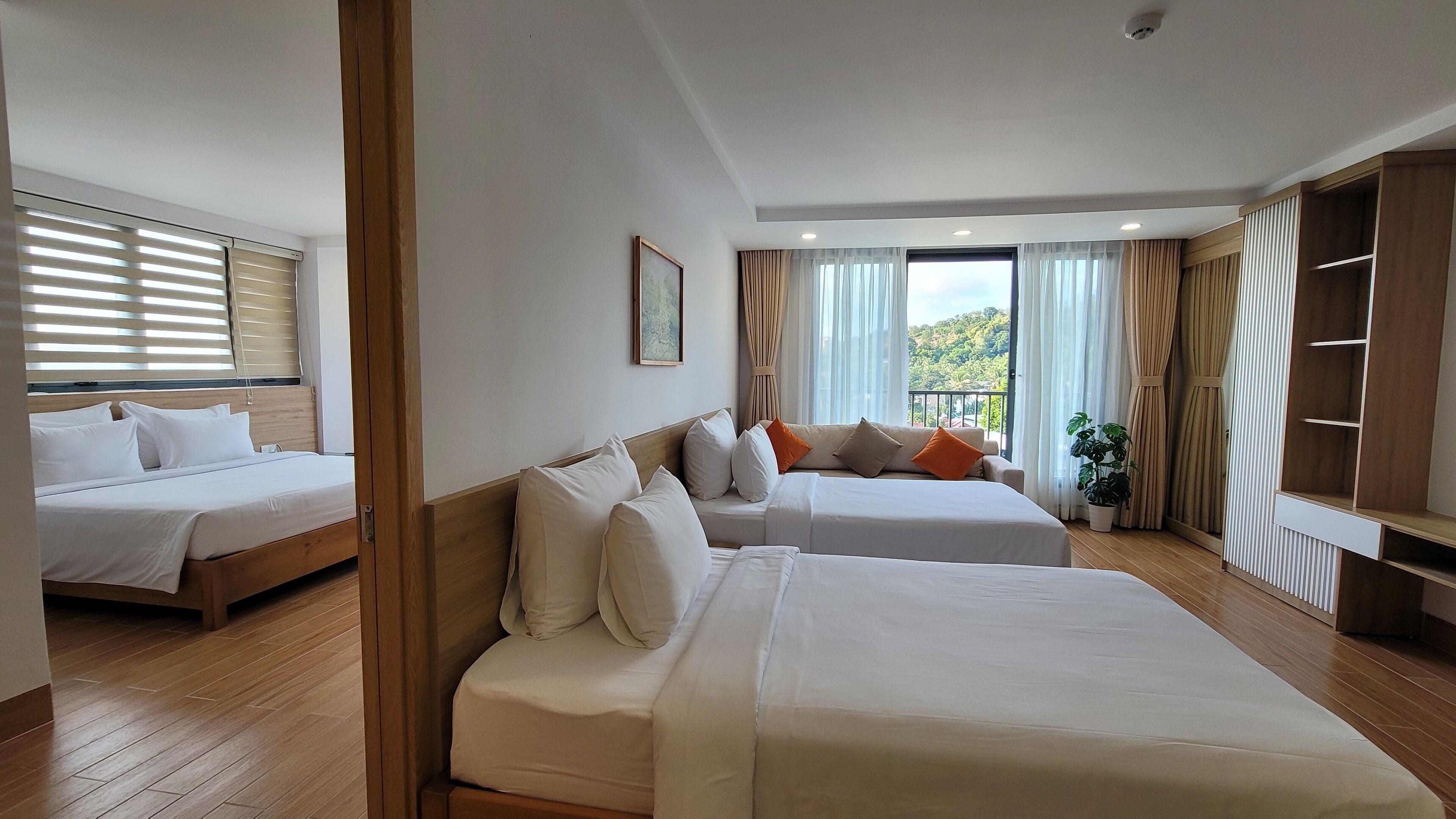A hotel room with two beds, a large window with curtains, a plant, and a wardrobe.