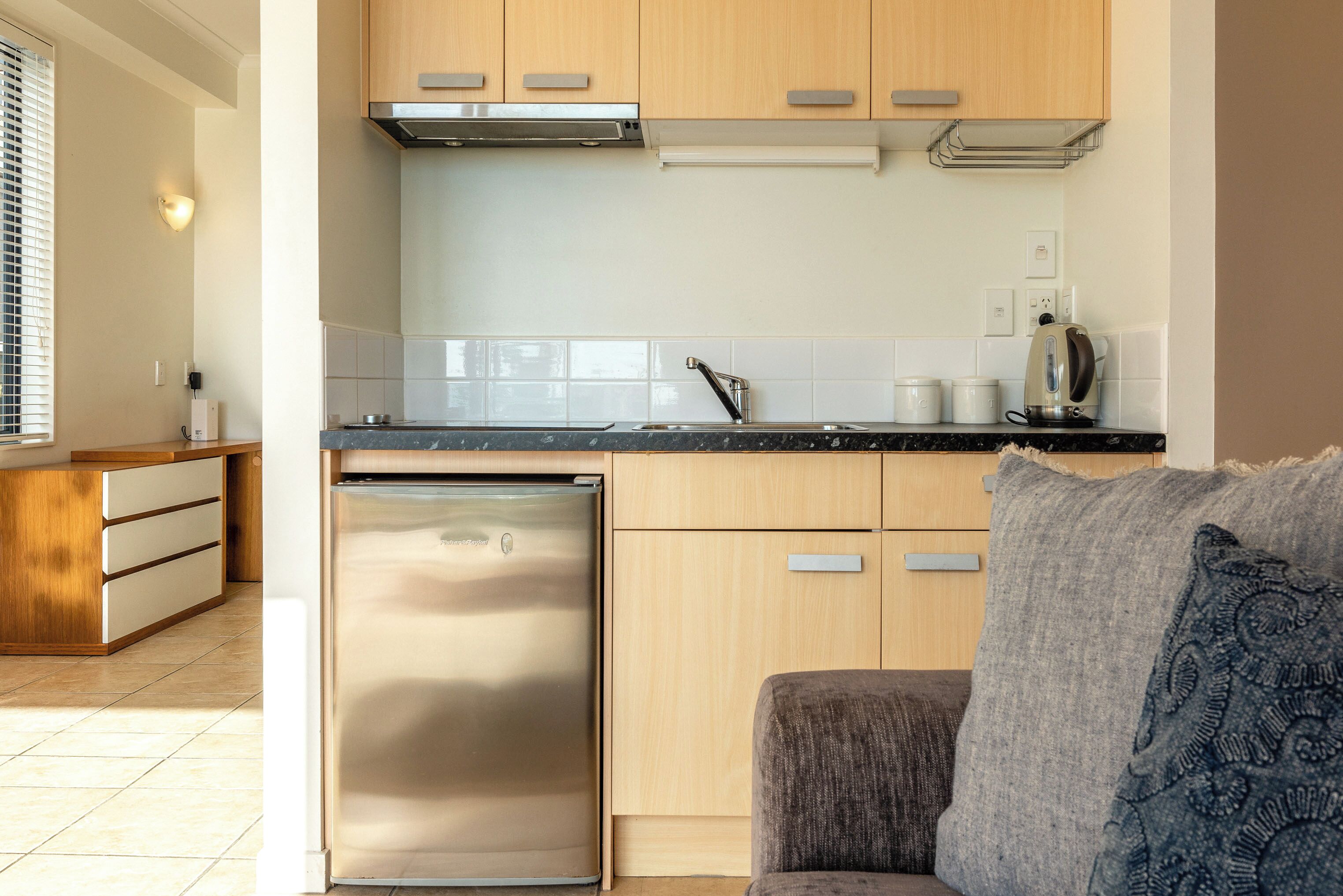 A modern kitchen with wooden cabinets, a stainless steel refrigerator, and a countertop with a kettle.