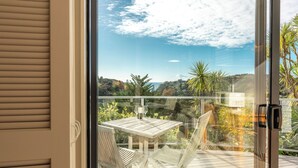 Un balcón con mesa y sillas de madera, con vista a un paisaje exuberante con árboles y cielo despejado.