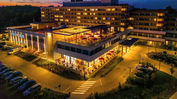A multi-story hotel with outdoor seating, a parking lot, and a pedestrian crossing.