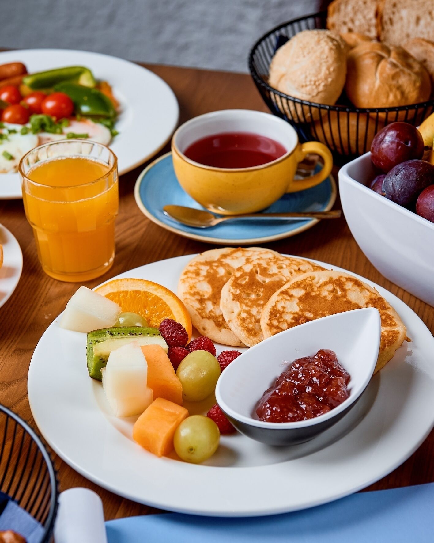 A breakfast setting with pancakes, fruit, jam, and a cup of tea.