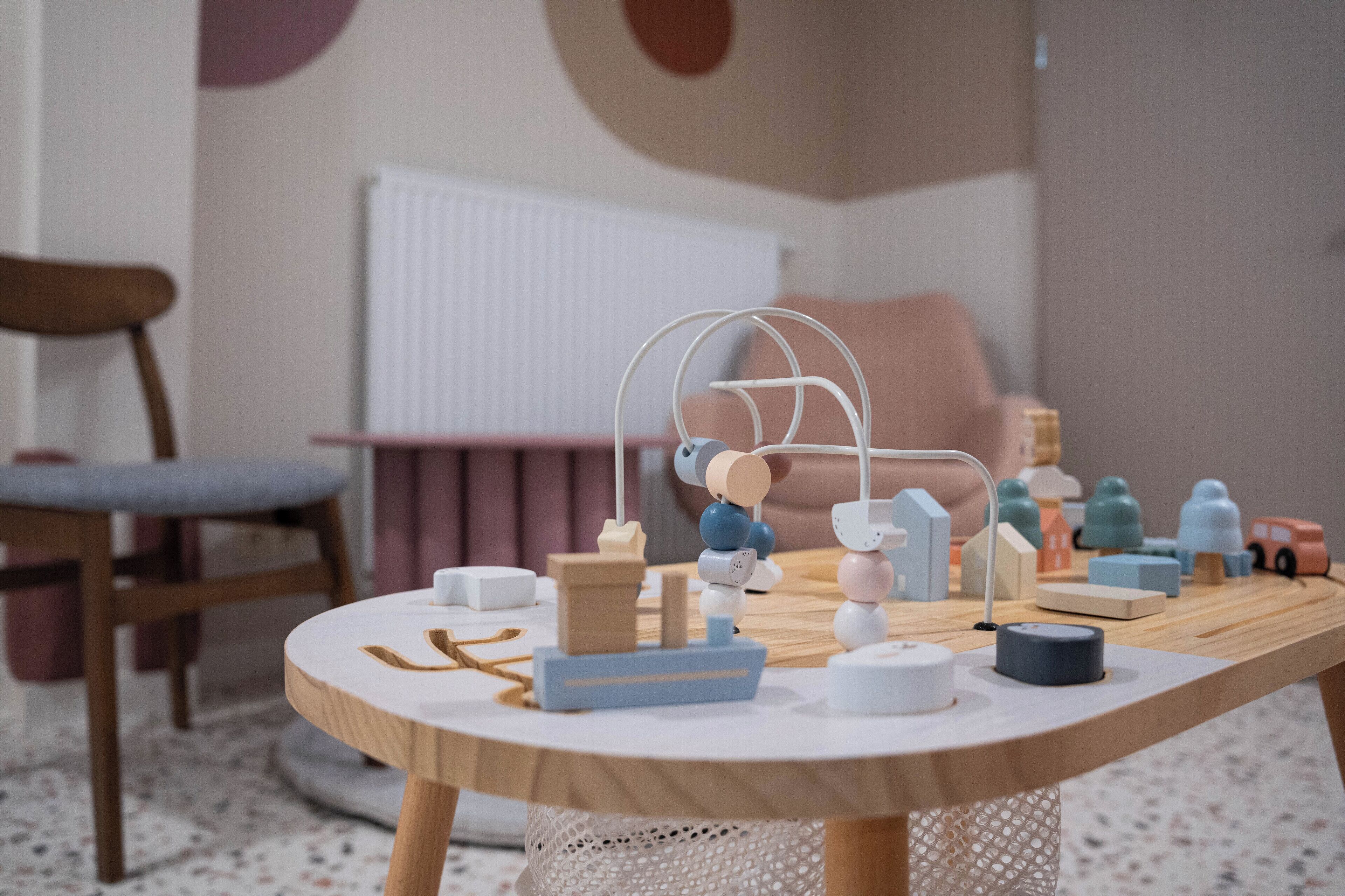Een ronde houten tafel met verschillende voorwerpen, waaronder een witte lamp, een blauw-wit speeltje en wat kleine blokken.