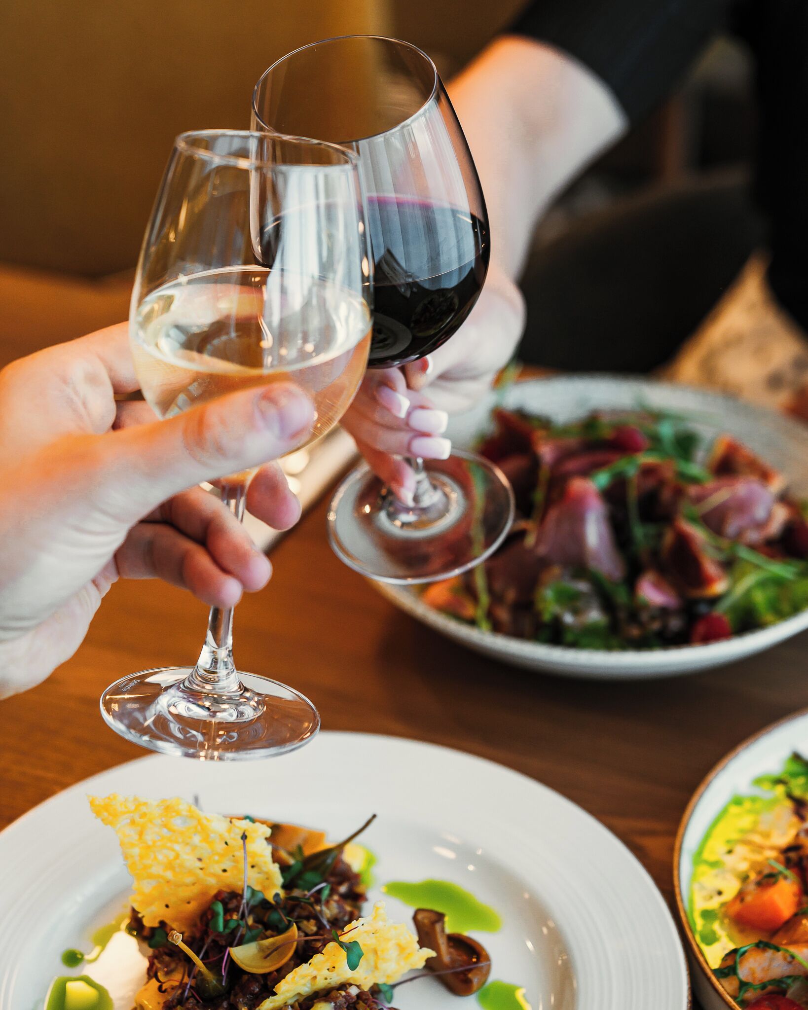 Une table à manger avec deux verres à vin, l’un rempli de vin blanc et l’autre de vin rouge, ainsi que des assiettes de nourriture.