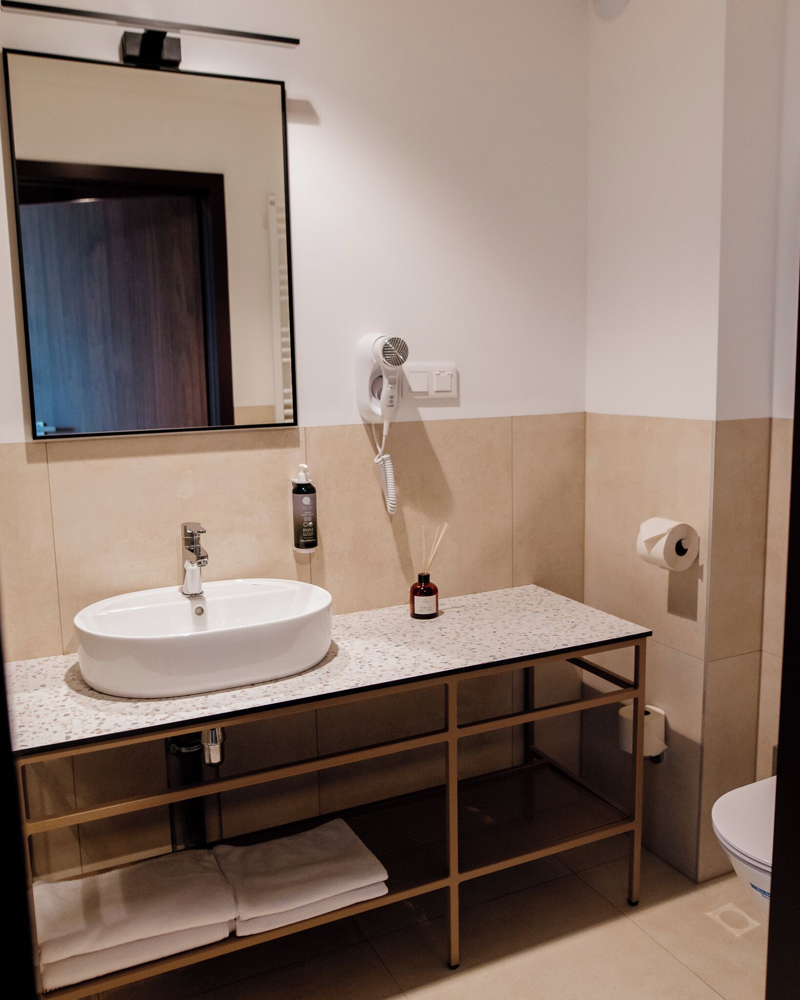 Une salle de bain avec un lavabo blanc, un miroir, un sèche-cheveux et des toilettes.