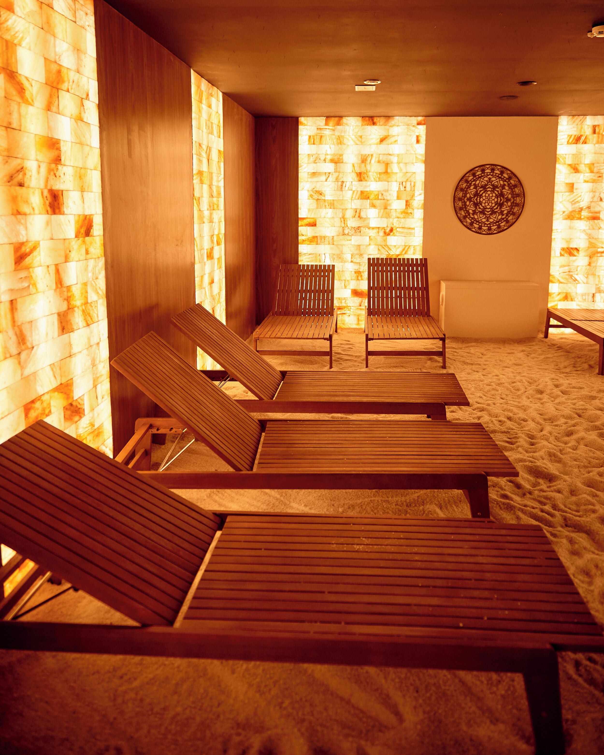 A spa area with wooden loungers, a wall with a geometric pattern, and a textured floor.