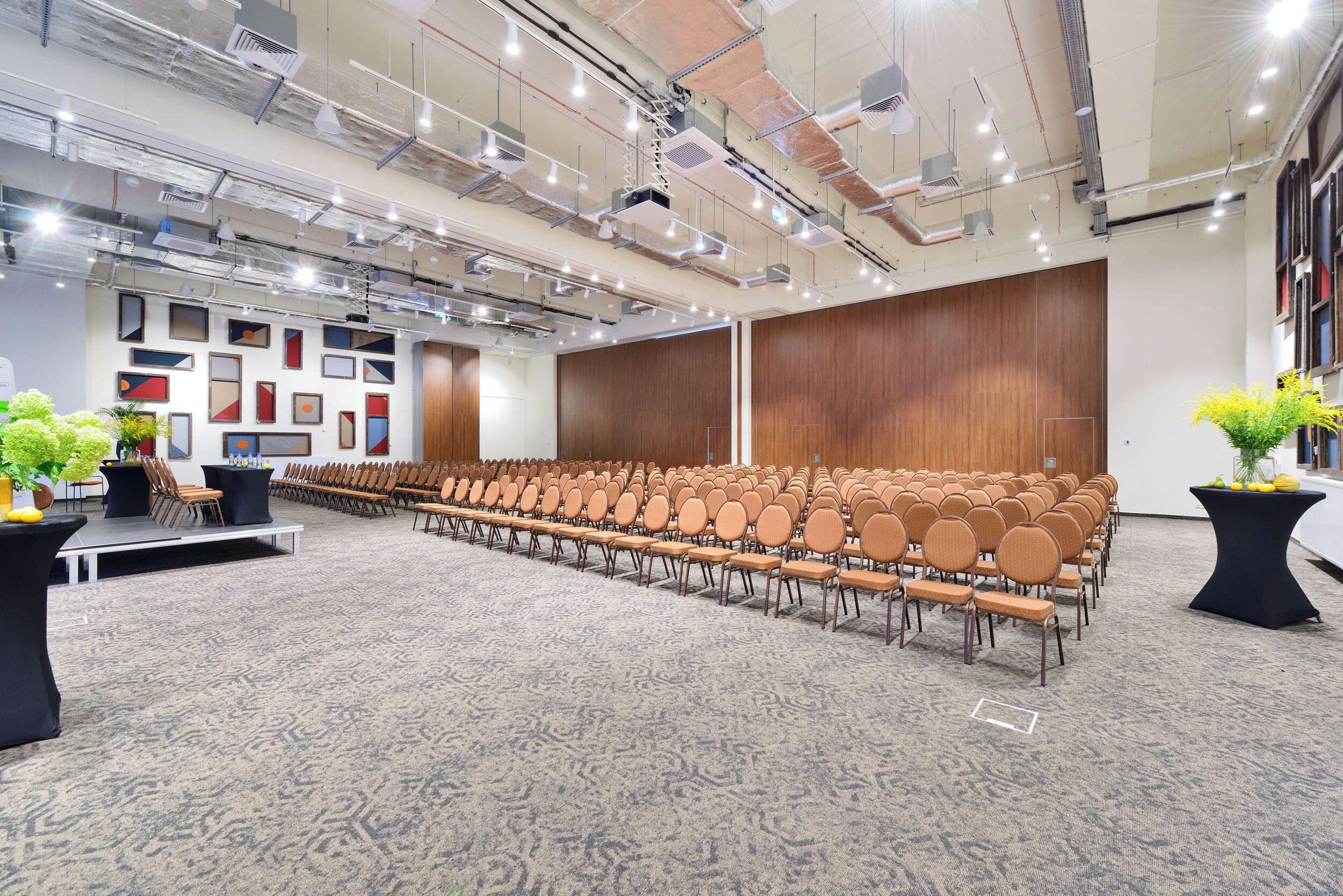 Une salle de conférence avec des rangées de chaises, une scène et un sol recouvert de moquette.