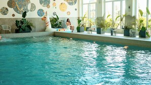 An indoor swimming pool with a mosaic wall, potted plants, and a chair.