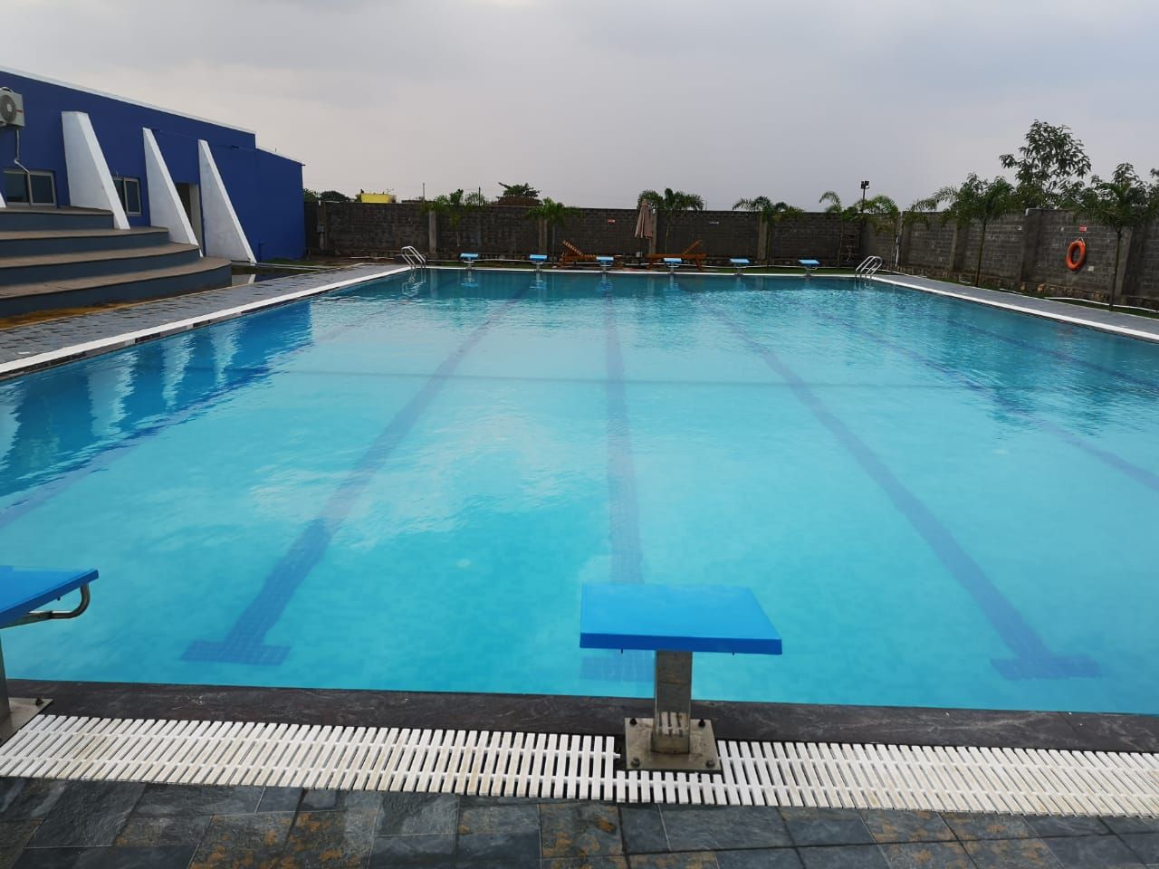A swimming pool with clear lane markings, a blue poolside area, and a stone wall in the background.