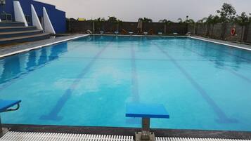 A swimming pool with clear lane markings, a blue poolside area, and a stone wall in the background.