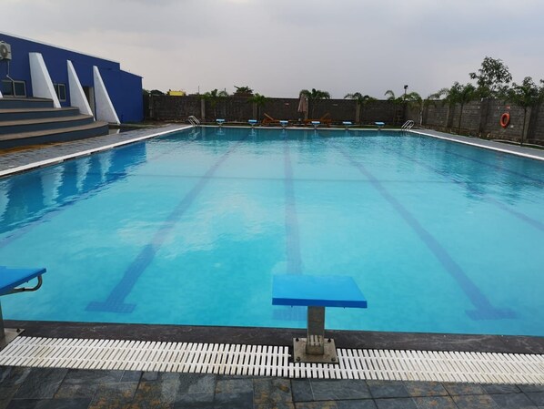 Piscina com faixas delimitadoras bem visíveis, área lateral azul e um muro de pedra ao fundo.
