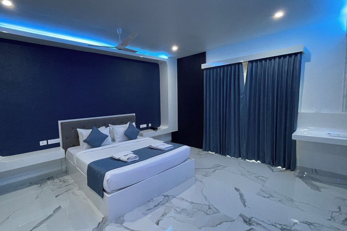 Quarto moderno com uma cama grande, um ventilador de teto e uma parede de destaque azul-escuro.