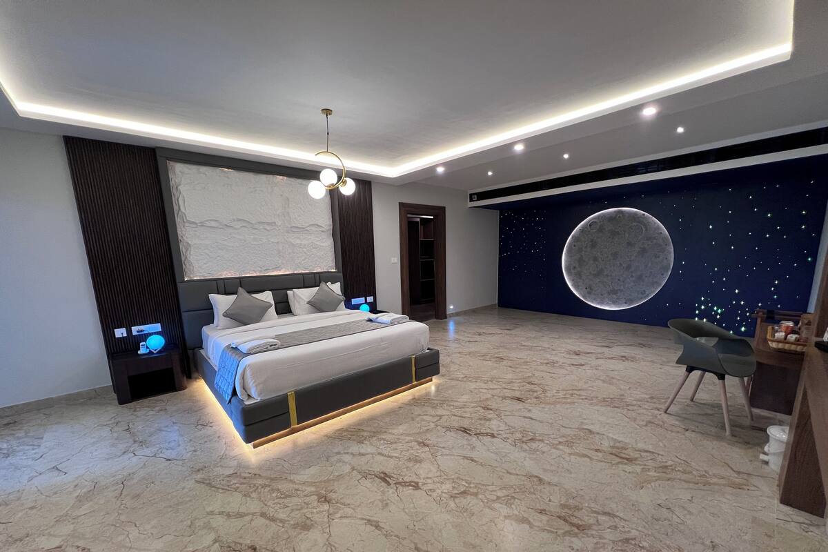 Une chambre moderne avec un grand lit, une fresque murale représentant la lune et un luminaire au plafond.