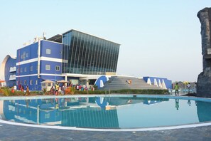 A modern hotel with a large pool area, a prominent glass building, and a staircase leading to an upper level. - Silver Stone Park Resort (Nagpur)