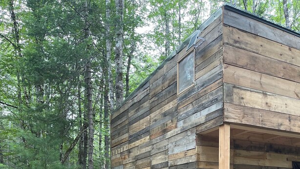 Eine rustikale Holzhütte mit geneigtem Dach, Holzfassade und einer kleinen Veranda.
