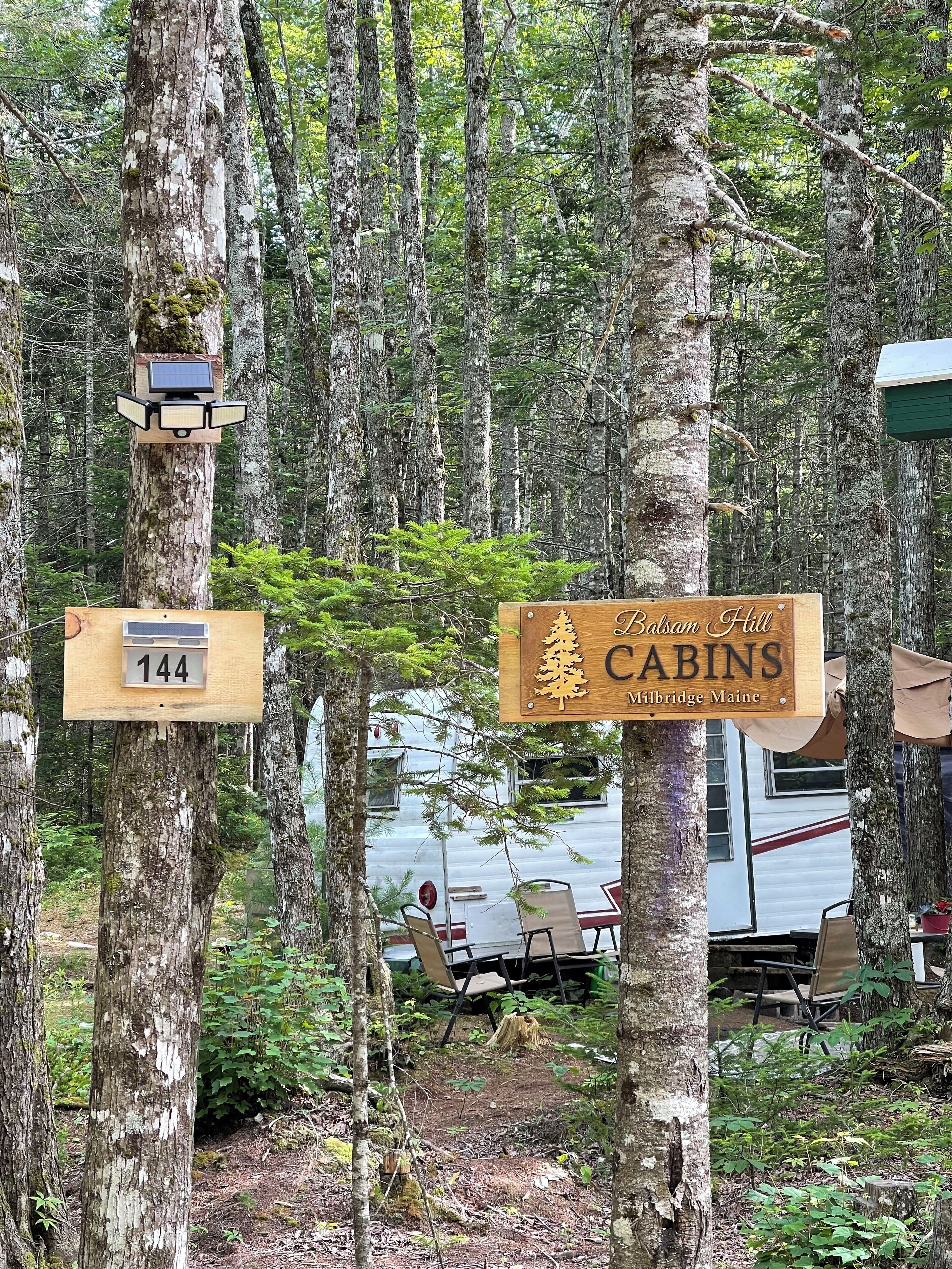 A wooden cabin sign with a pine tree logo and the text "Balsam Hill Cabins Milbridge Maine".