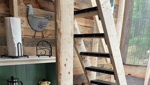 Ein rustikaler Holzinnenraum mit einer Holzleiter, Regalen mit verschiedenen Gegenständen und einem kleinen Holzstuhl.