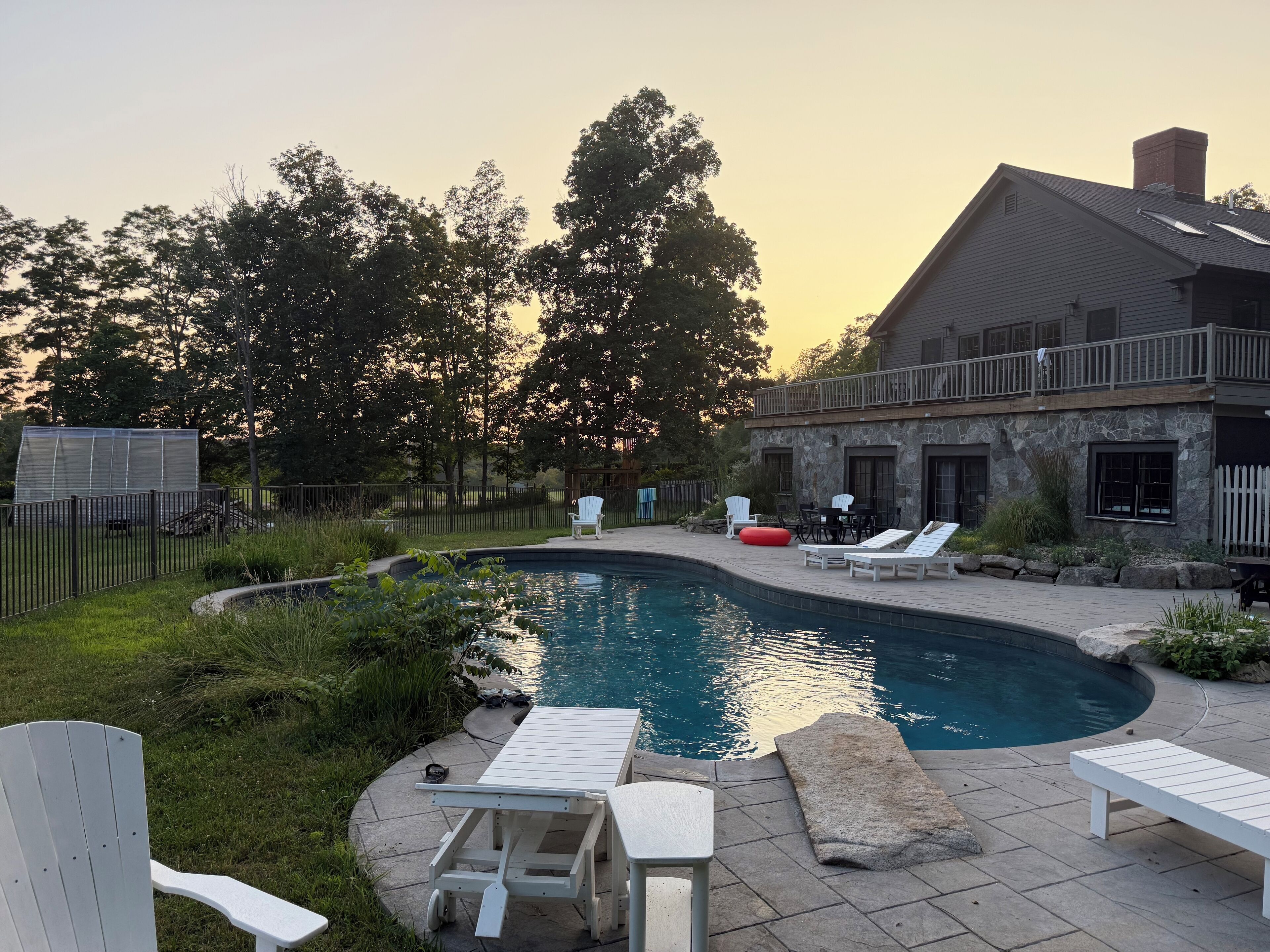 A swimming pool with lounge chairs and a table, surrounded by a stone patio and a stone building with a balcony.