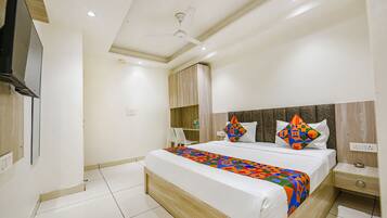 A modern hotel room with a large bed, a ceiling fan, a TV mounted on the wall, and a bedside table with a lamp.