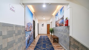 A hallway with a patterned carpet, tiled walls, and a fire extinguisher on the right. - Via Sunset Residency (Navi Mumbai)