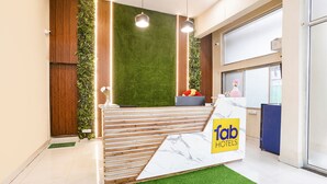 A reception desk with a 'Tab Hotels' sign, a green artificial grass area, wooden slats, and a vertical garden. - Via Sunset Residency (Navi Mumbai)