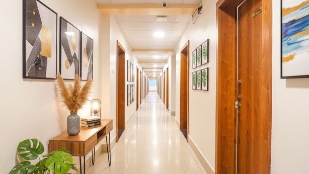 A hotel hallway with framed artwork on the walls, a wooden reception desk, and a potted plant. - FabHotel Embassy (Pune)