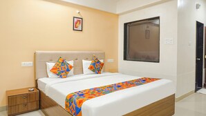 A neatly made bed with a colorful blanket, a bedside table with drawers, and a wall-mounted picture. - FabHotel Embassy (Pune)