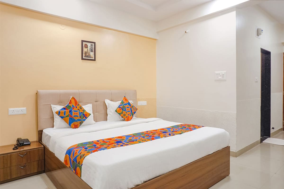 A neatly made bed with a colorful geometric-patterned bedspread, a wooden nightstand with a telephone, and a wall-mounted picture.